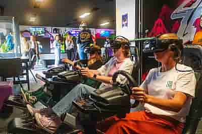 A group of three people racing in Valve Index headsets on a racing simulator using Logitech steering wheel and pedals during a company outing
