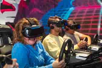 A group of three people smiling and racing on a Formula 1 simulator in Valve Index headsets during a bachelor's party