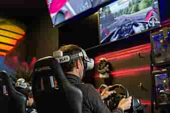 A group of people racing on a racing simulator in Valve Index headset with 4 TV screens broadcasting their race on the wall