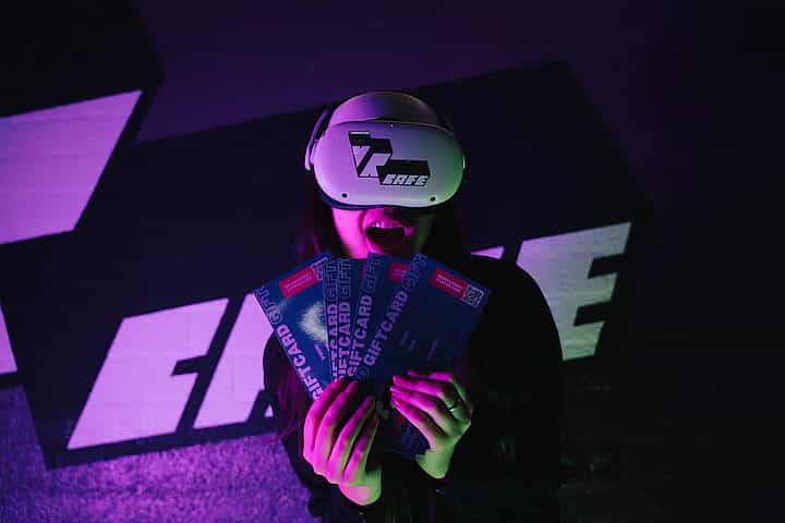 Woman in Meta Quest 2 headset holding 5 VRcafe Haarlem giftcards