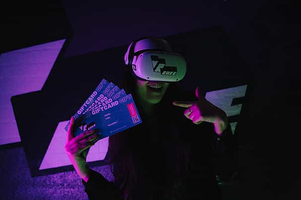 Woman in Meta Quest 2 headset with VRcafe Haarlem logo sticker on it holding 3 giftcards