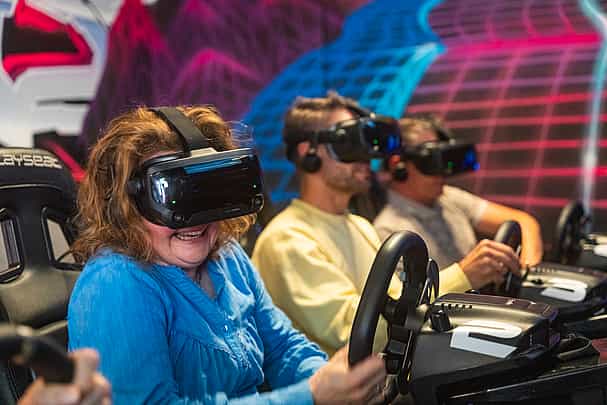A group of three people smiling and racing on a Formula 1 simulator in Valve Index headsets during a bachelor's party