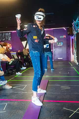 A woman standing on a plank while wearing a Meta Quest 2 headset during a company outing at VRcafe Haarlem