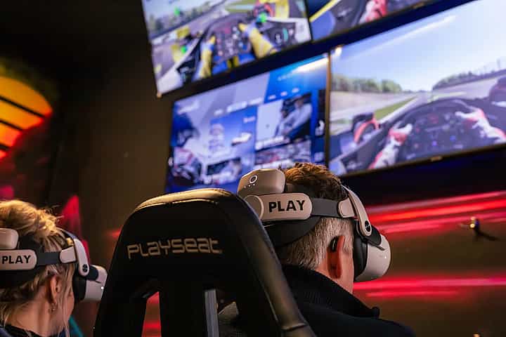 Two people racing on a Formula 1 simulator in Meta Quest 2 headsets during a company outing