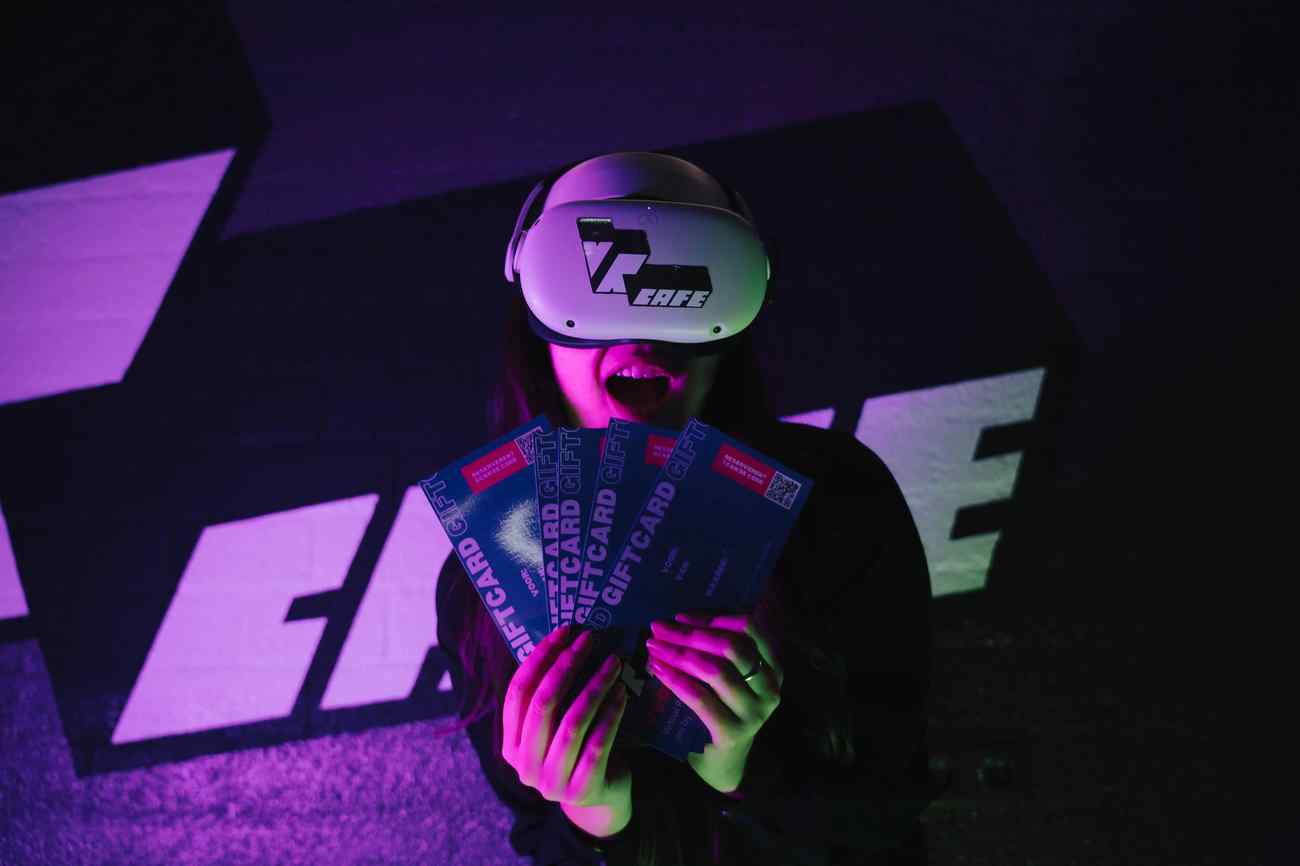 Woman in Meta Quest 2 headset holding 5 VRcafe Haarlem giftcards