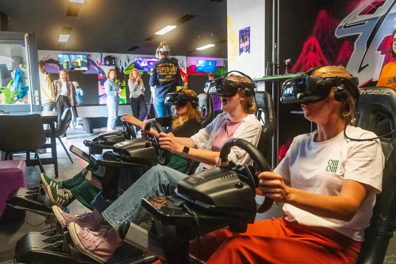 A group of three people racing in Valve Index headsets on a racing simulator using Logitech steering wheel and pedals during a company outing