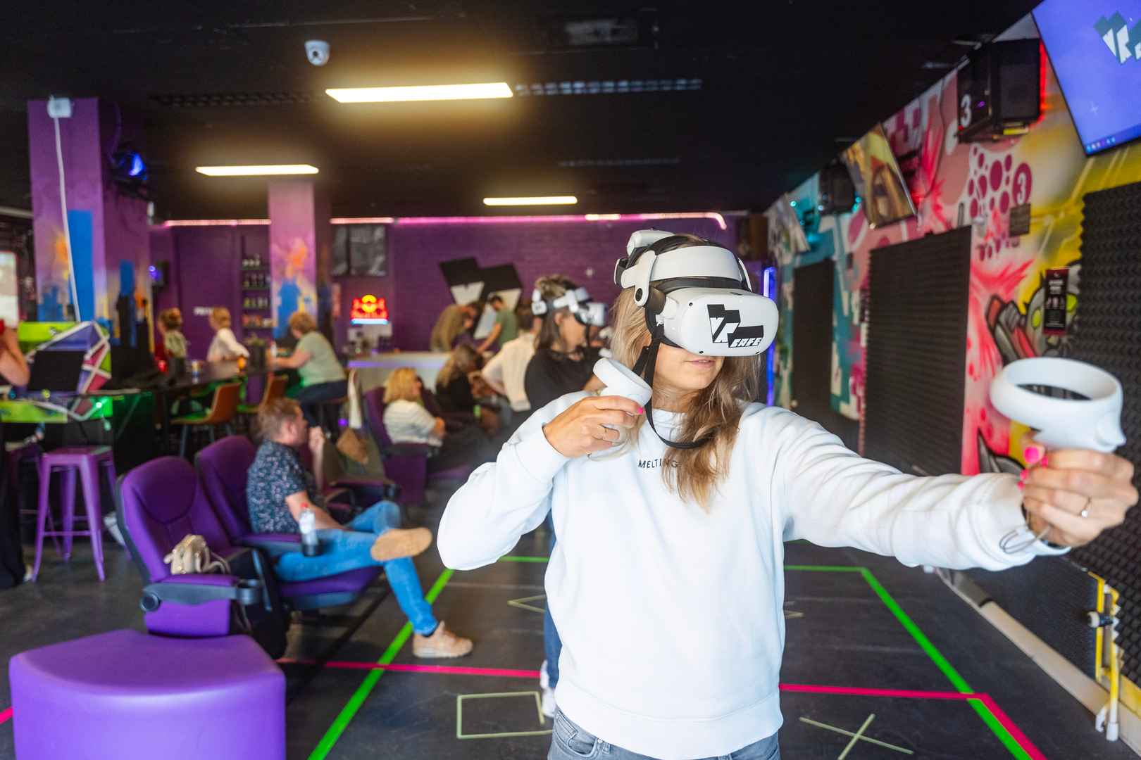 Woman playing Elven Assasin in Meta Quest 2 headset during a busy company outing happening behind her in real live at VRcafe Haarlem