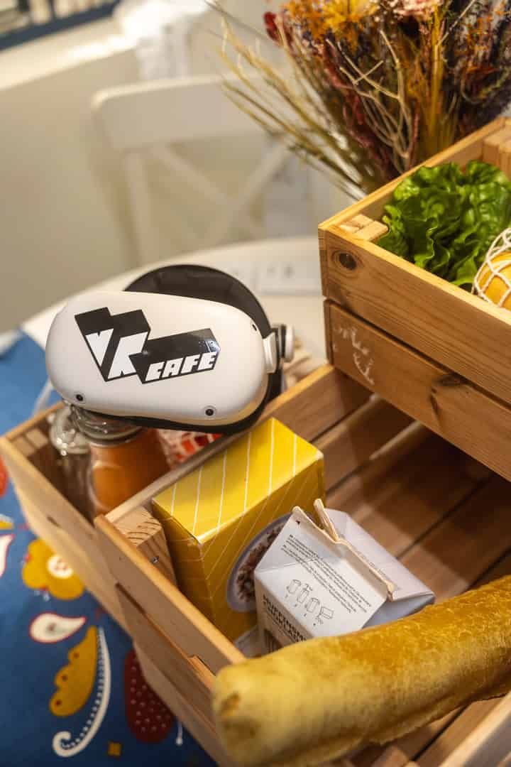 Meta Quest 2 headset with VRcafe Haarlem logo sticker on it laying on a wooden box with kitchen items and foods