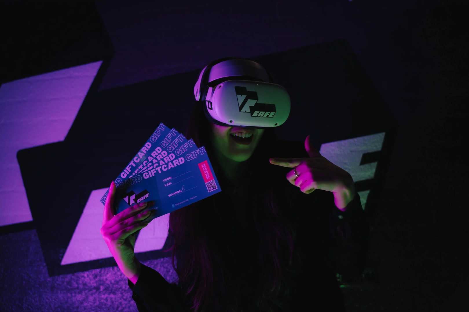 Woman in Meta Quest 2 headset with VRcafe Haarlem logo sticker on it holding 3 giftcards